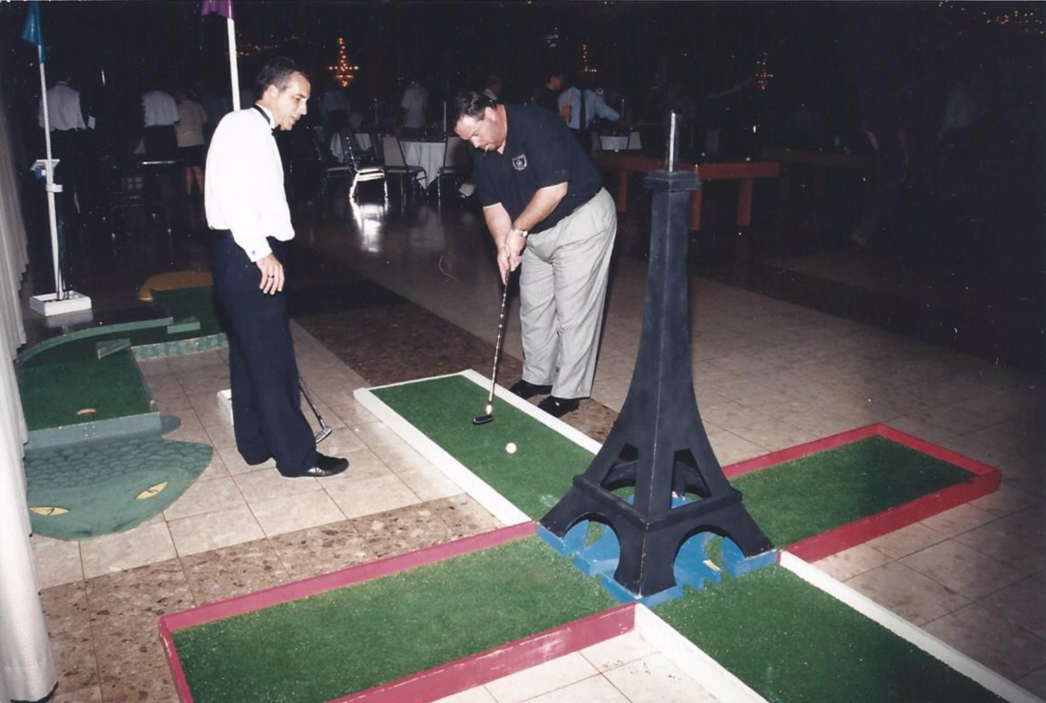 Two men are playing miniature golf in front of an eiffel tower