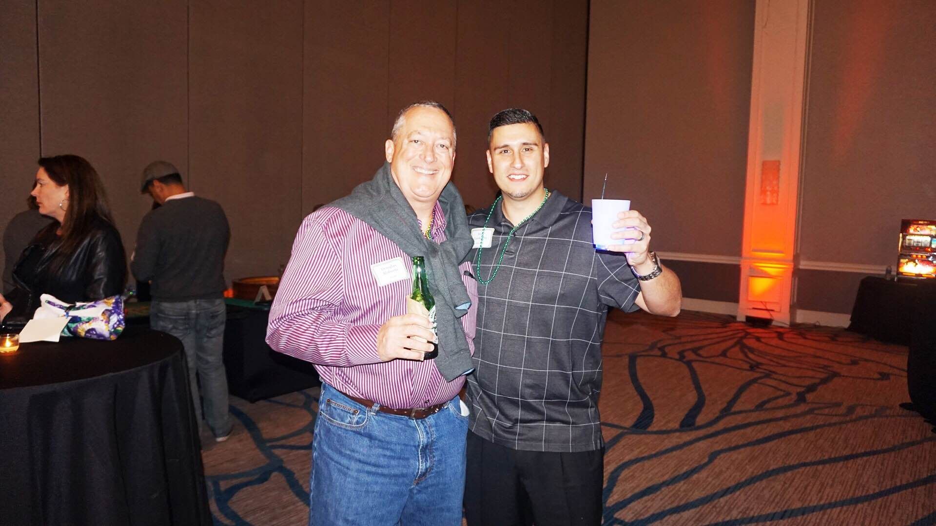 Two men are standing next to each other in a room holding drinks.