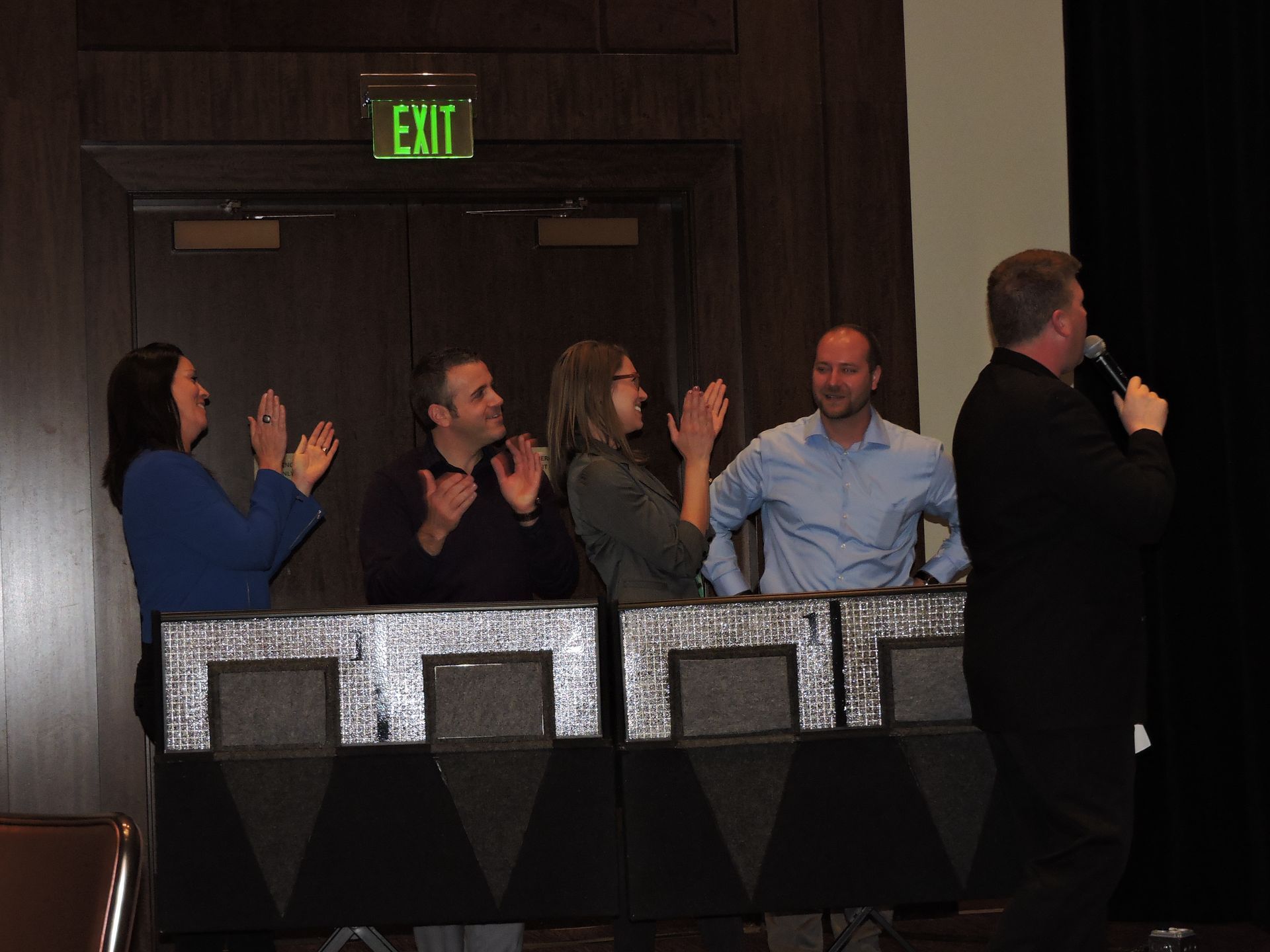 A group of people are clapping in front of an exit sign