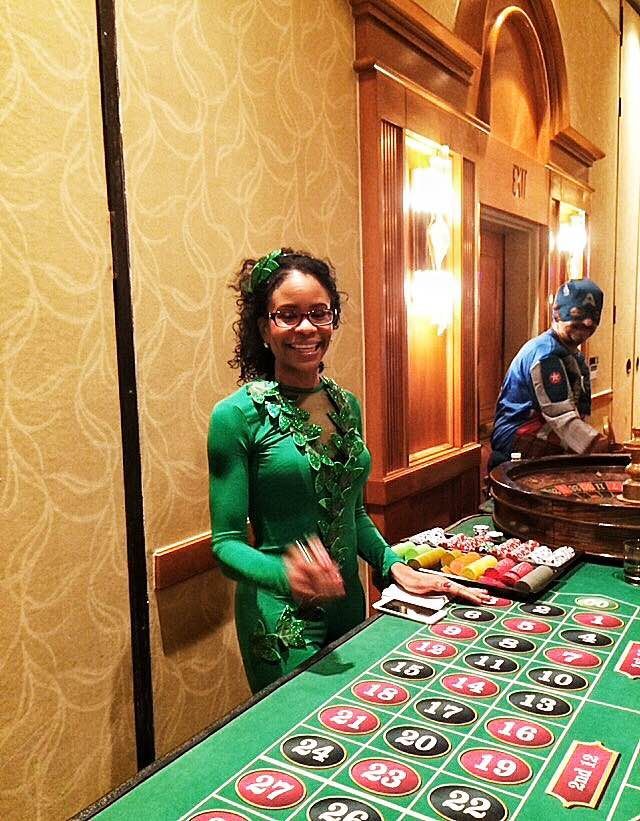 A woman in a green outfit is standing in front of a roulette table.