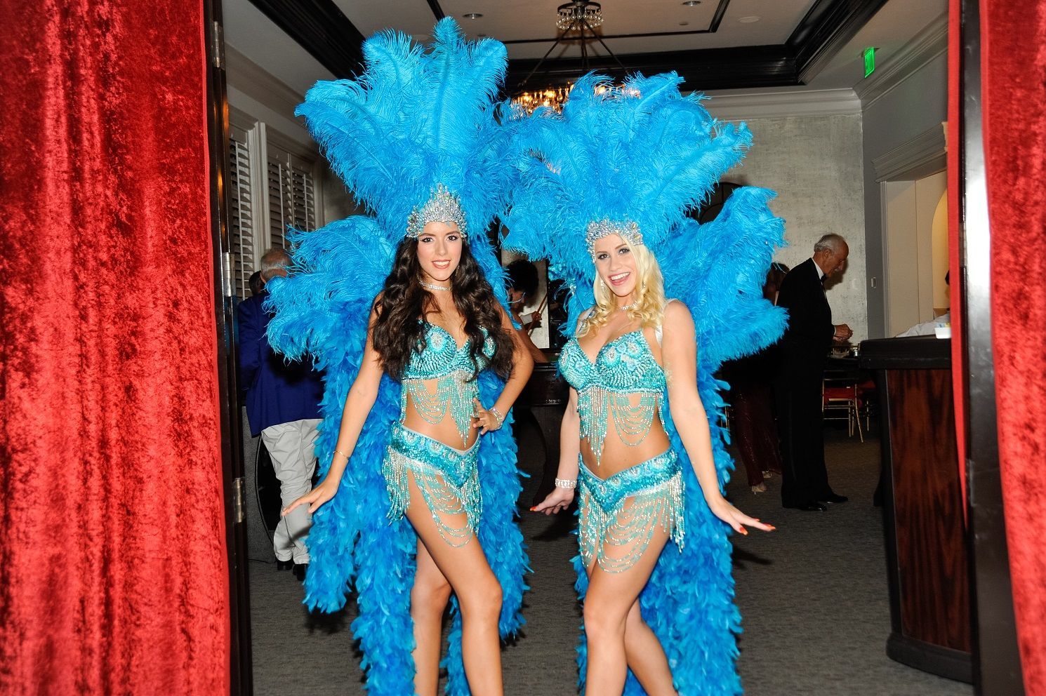 Two women in blue feathered costumes are walking through a doorway.