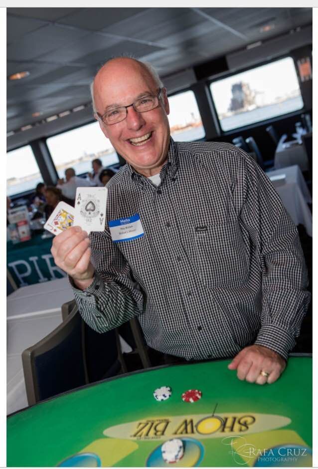 A man is holding a pair of cards in front of a poker table.