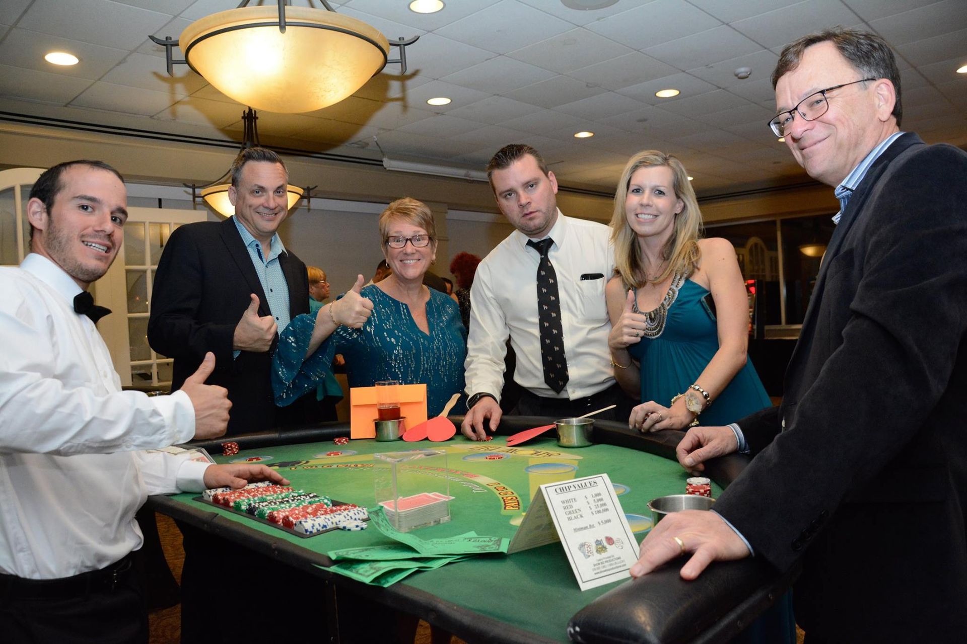 A group of people are standing around a roulette table giving thumbs up.