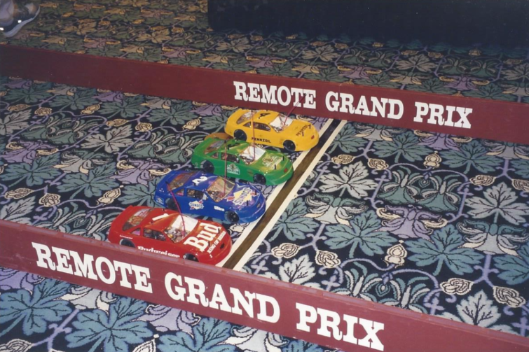 A bunch of toy cars are on a track that says remote grand prix
