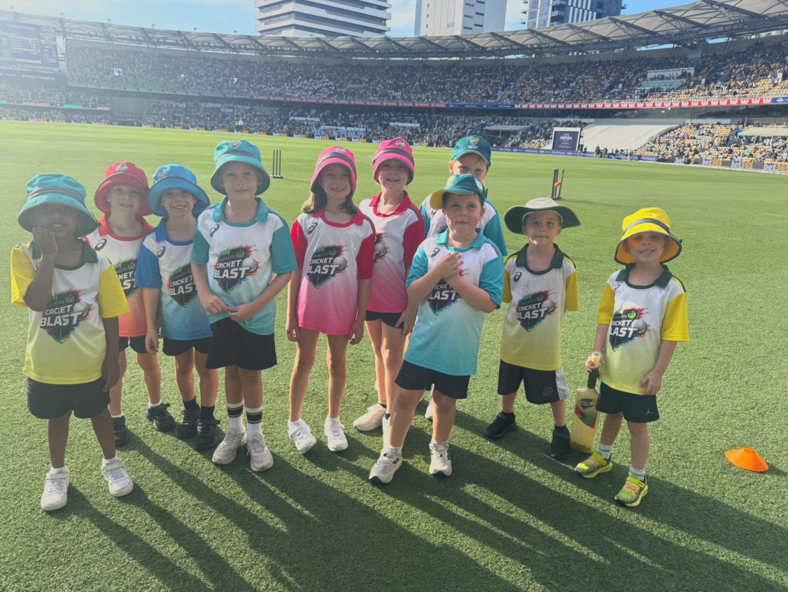 Children in colorful hats posing on a sports field with stadium seating in the background