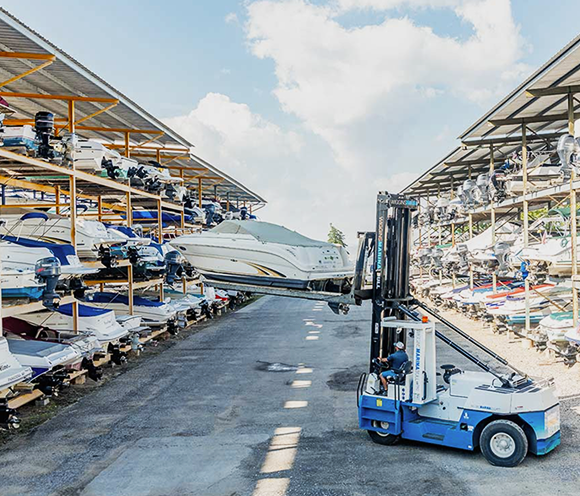 A forklift lifting a boat from a rack at a boat storage facility. Blue skies, many boats.