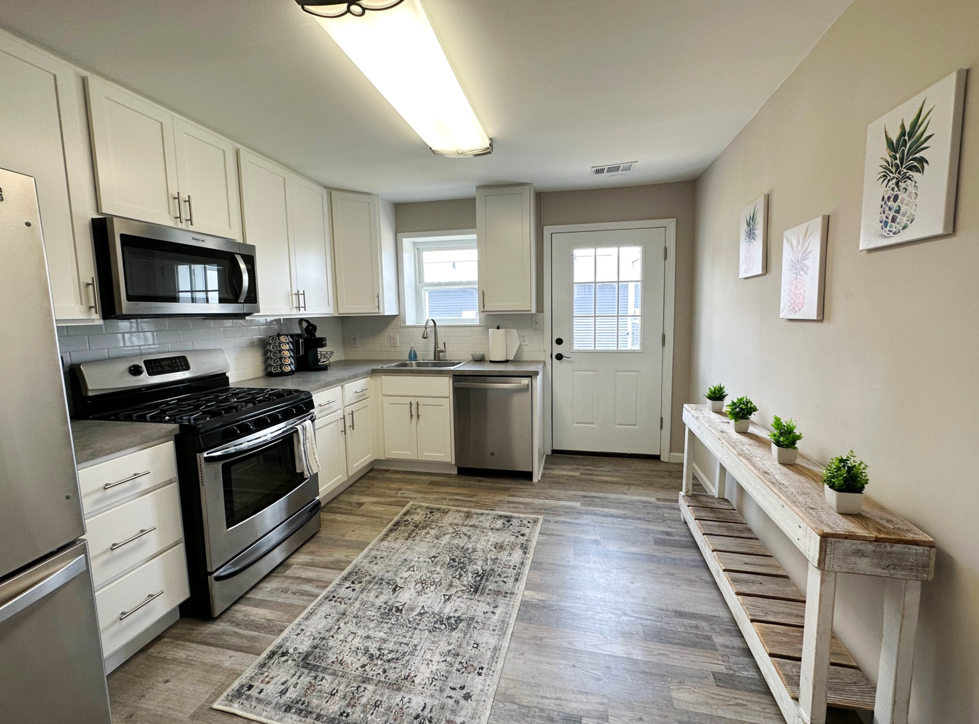 Bright kitchen with white cabinets, stainless steel appliances, and a gray rug.
