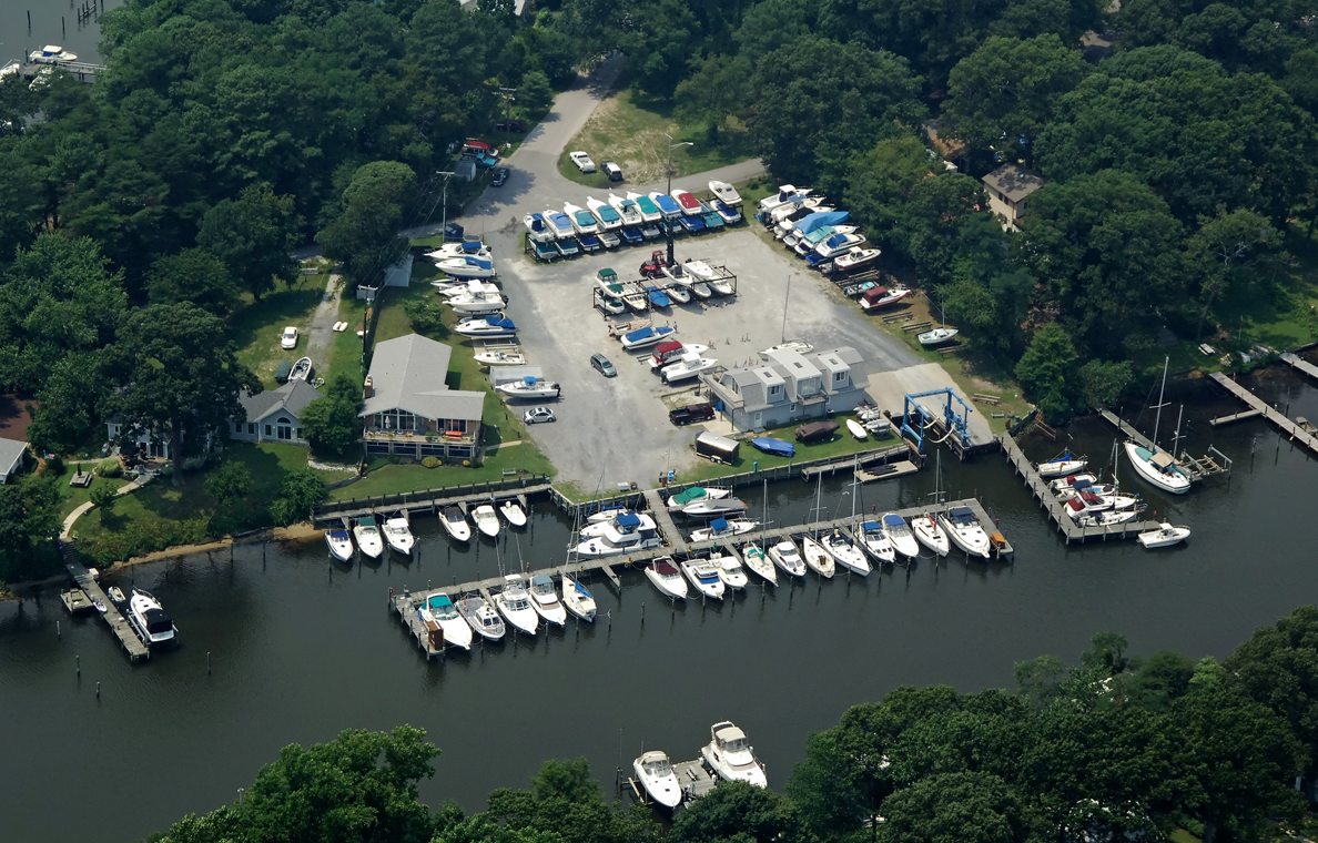 Aerial view of a marina with boats docked, boat storage, and surrounding trees.