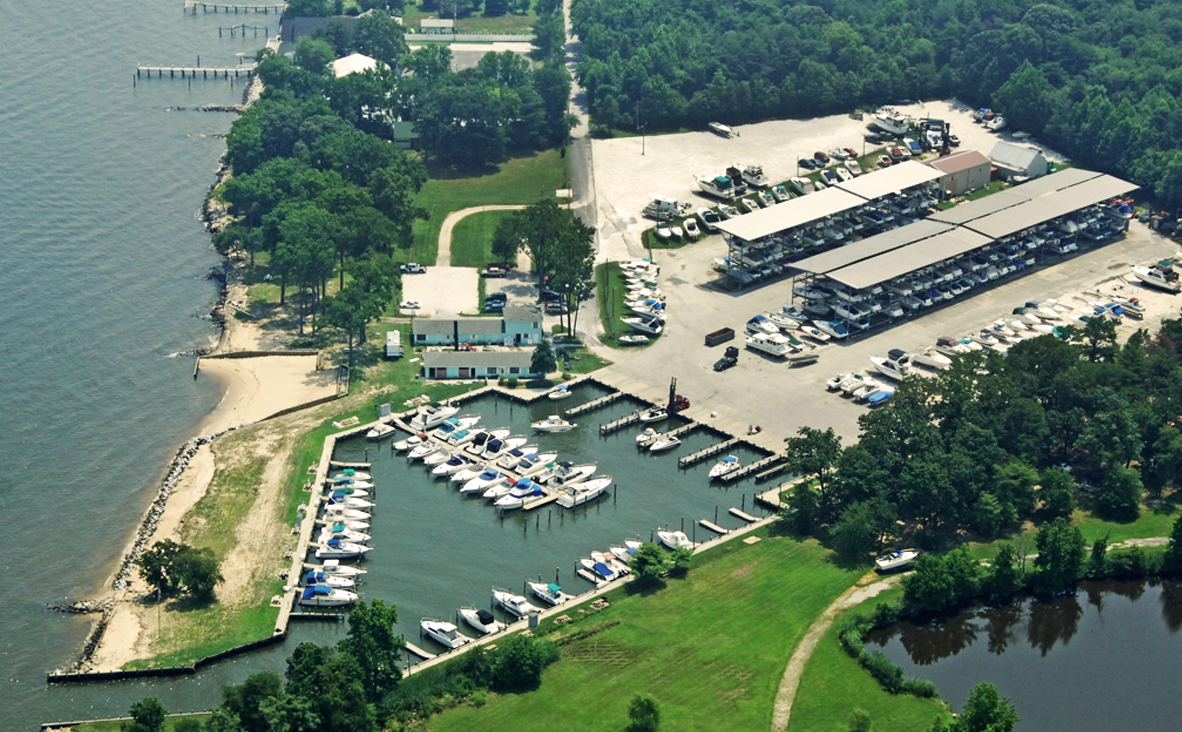 Aerial view of a marina with docks, boats, storage buildings, and a sandy shoreline.