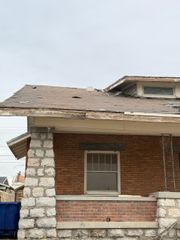 Damaged brick house with a partially collapsed roof and a blue trash bin beside it