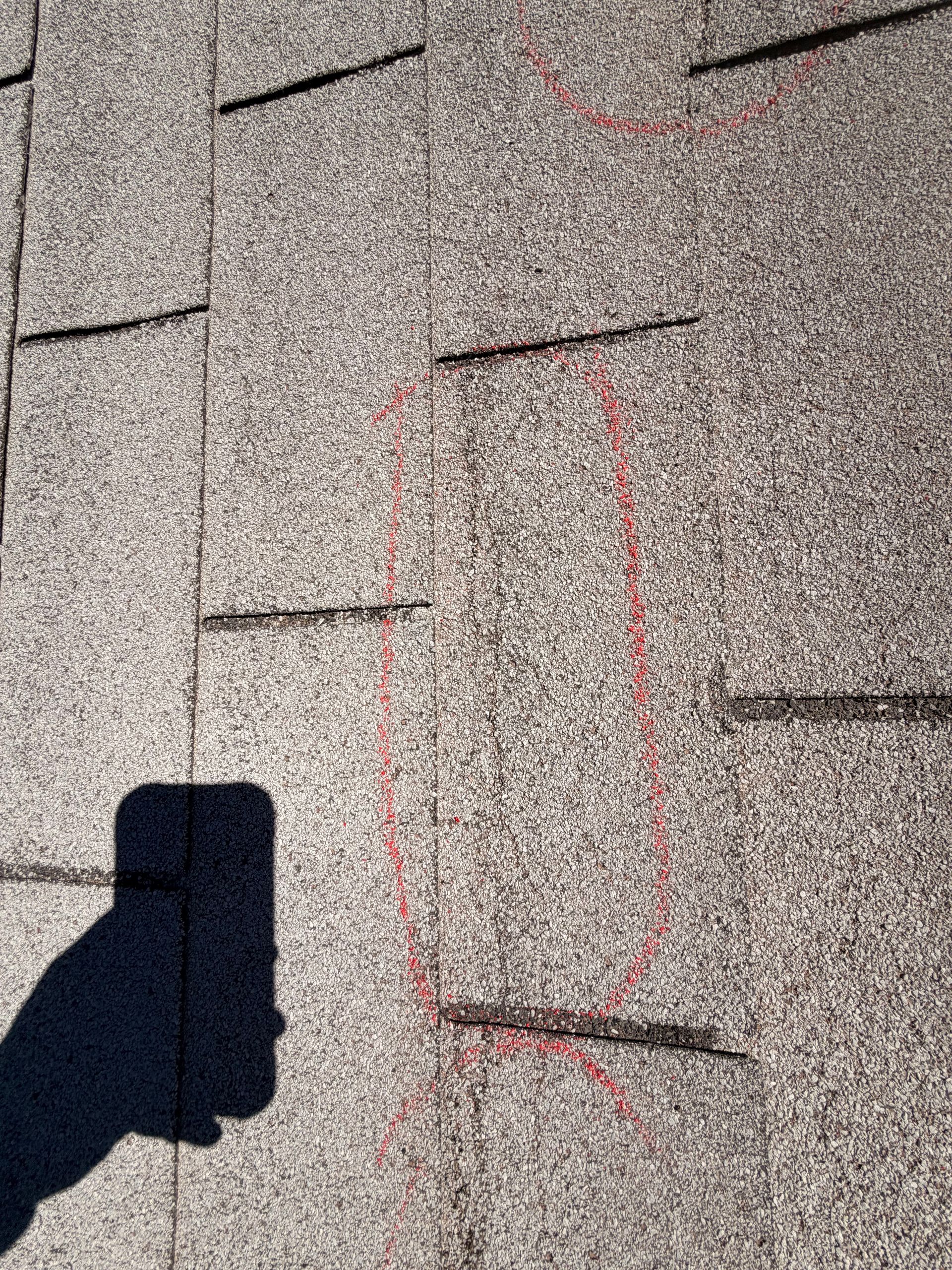 Close-up of gray roof shingles with red chalk markings and a shadow at lower left.