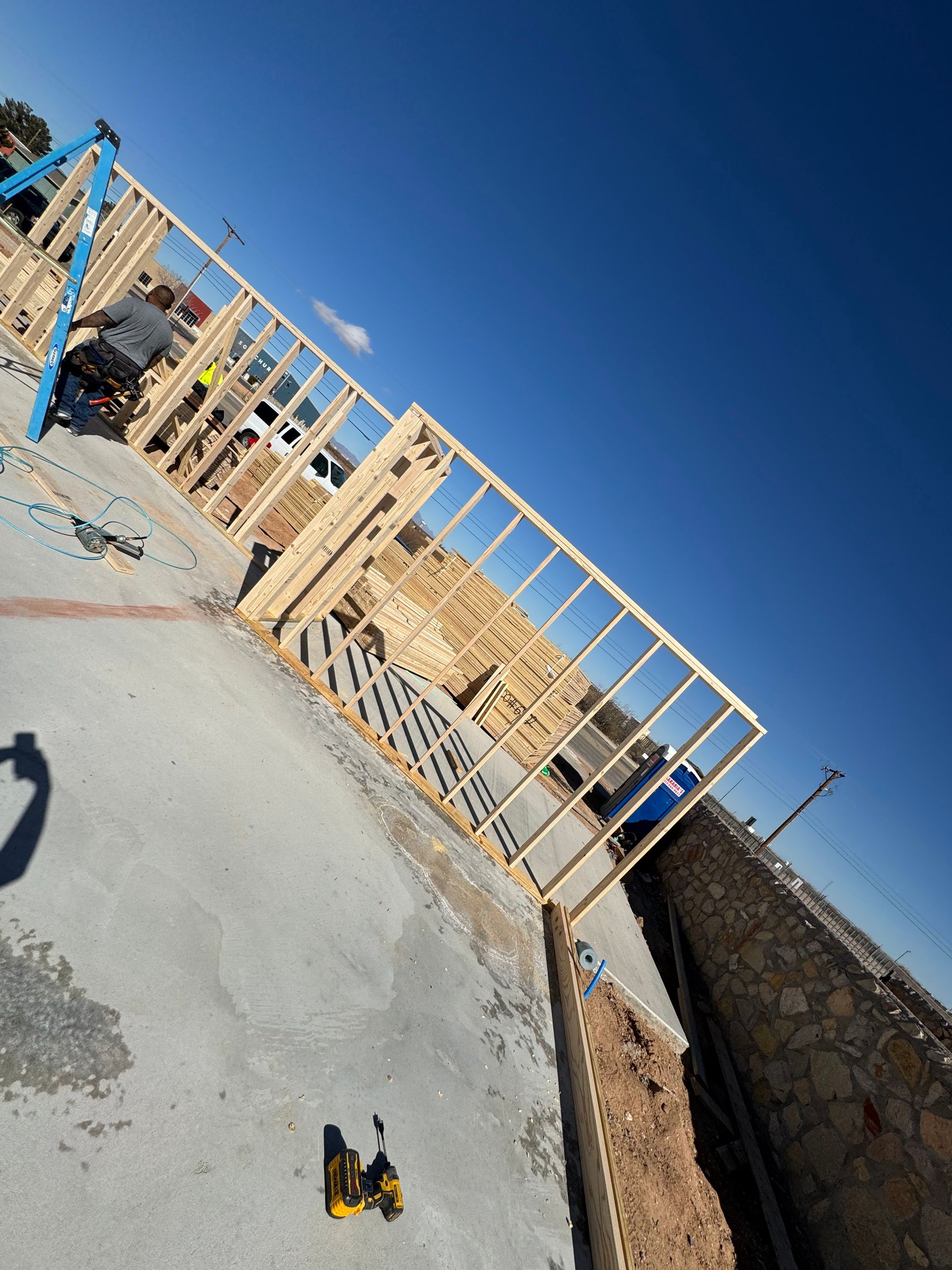 Tilted view of a construction site with wooden framing, concrete walls, and a bright blue sky.