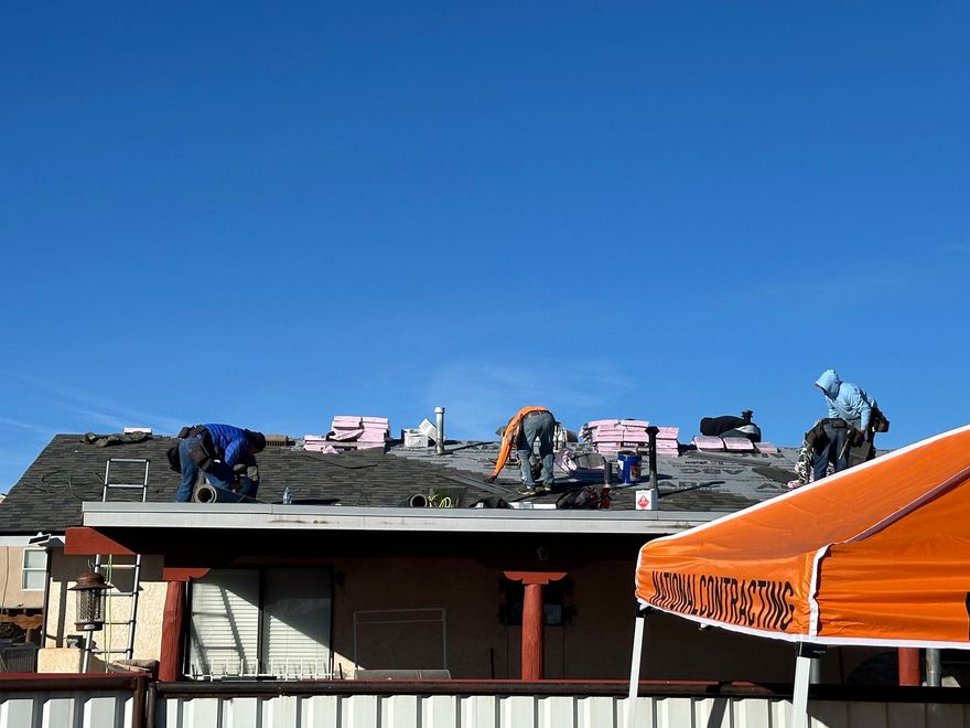 Workers repairing a roof with pink insulation under a clear blue sky, orange canopy in foreground
