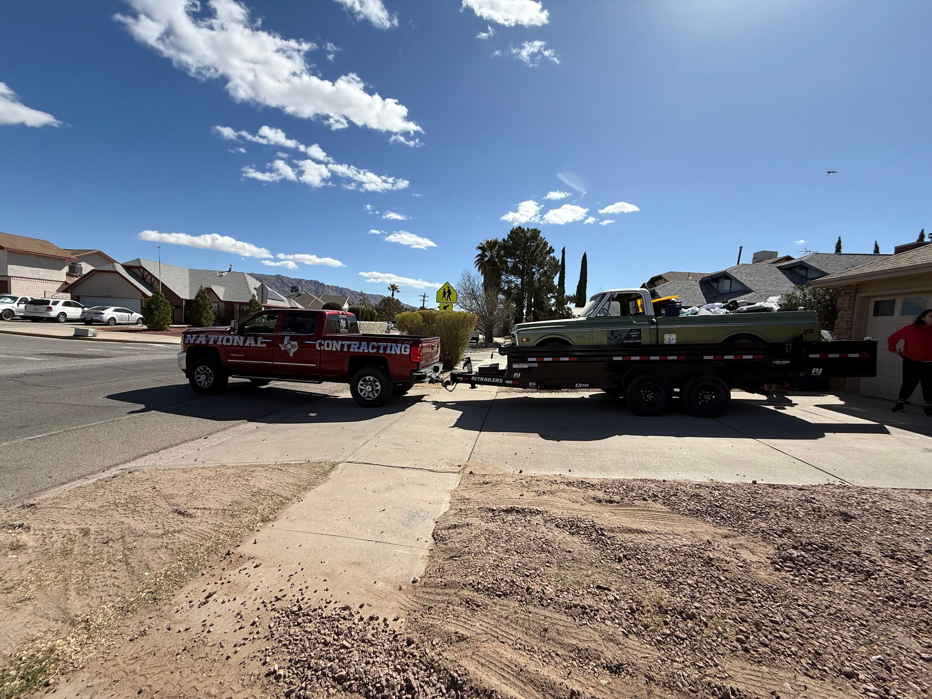 Two tow trucks parked side by side on a sunny suburban street under a blue sky.