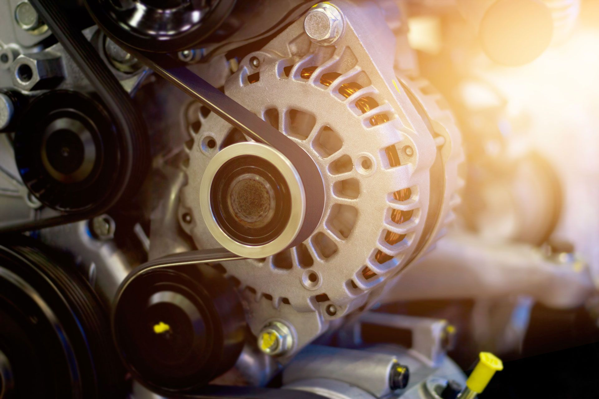 Alternator with belt in a vehicle engine, with a yellow light source.