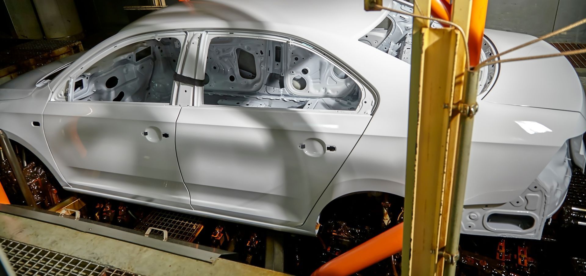 A person uses a tool to fix a dent in a black car, lit by a fluorescent light in a workshop. A person uses a tool to fix a dent in a black car, lit by a fluorescent light in a workshop.