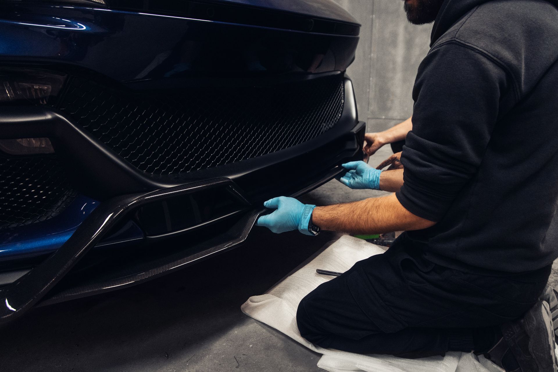 Mechanic in gray gloves using a wrench on a car engine in a garage.