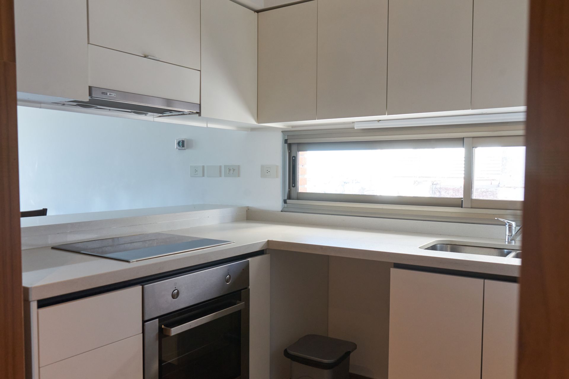 Cocina moderna y blanca con horno empotrado, placa de cocina, fregadero y armarios altos.