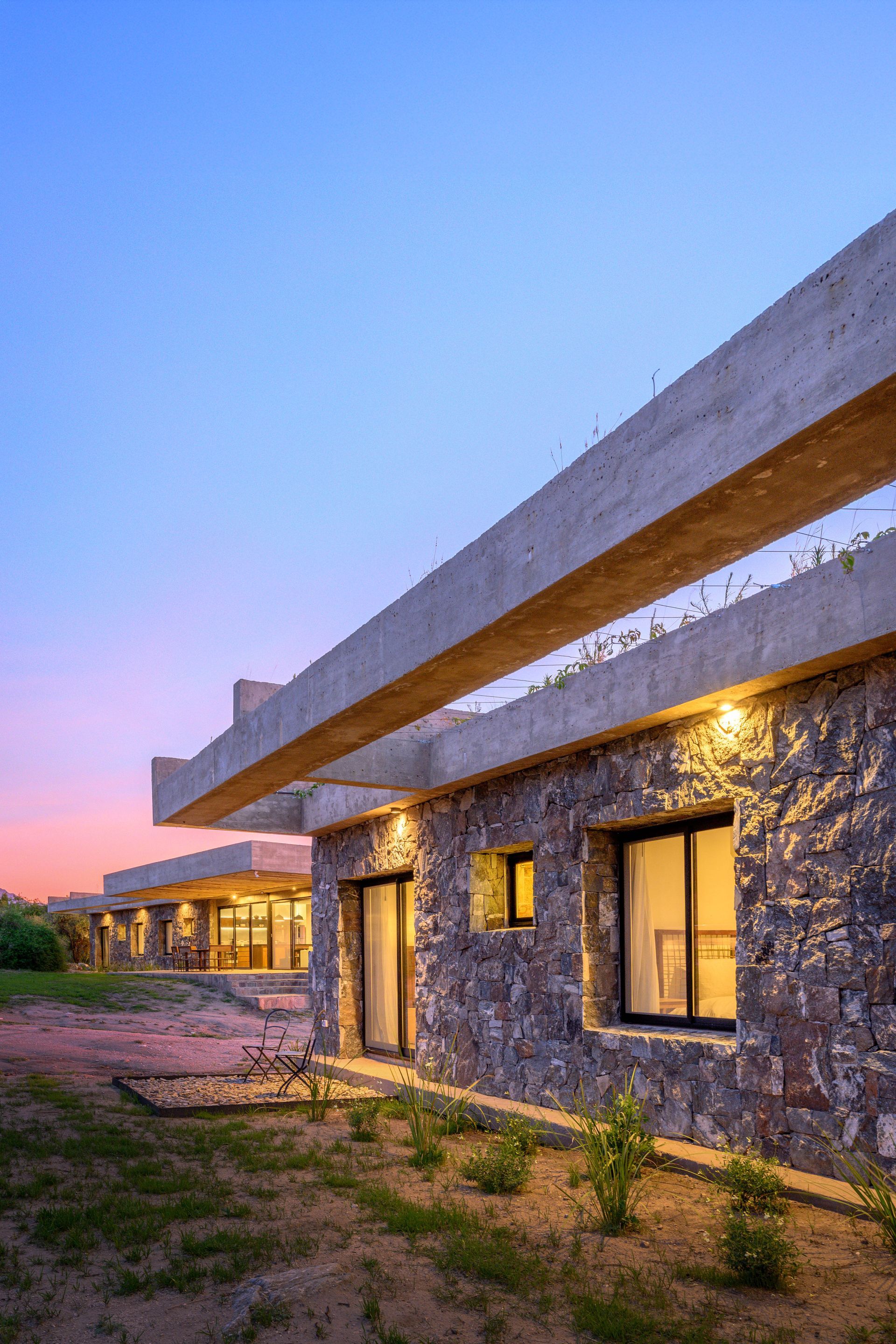 Edificio con paredes de piedra y voladizo de hormigón al anochecer.