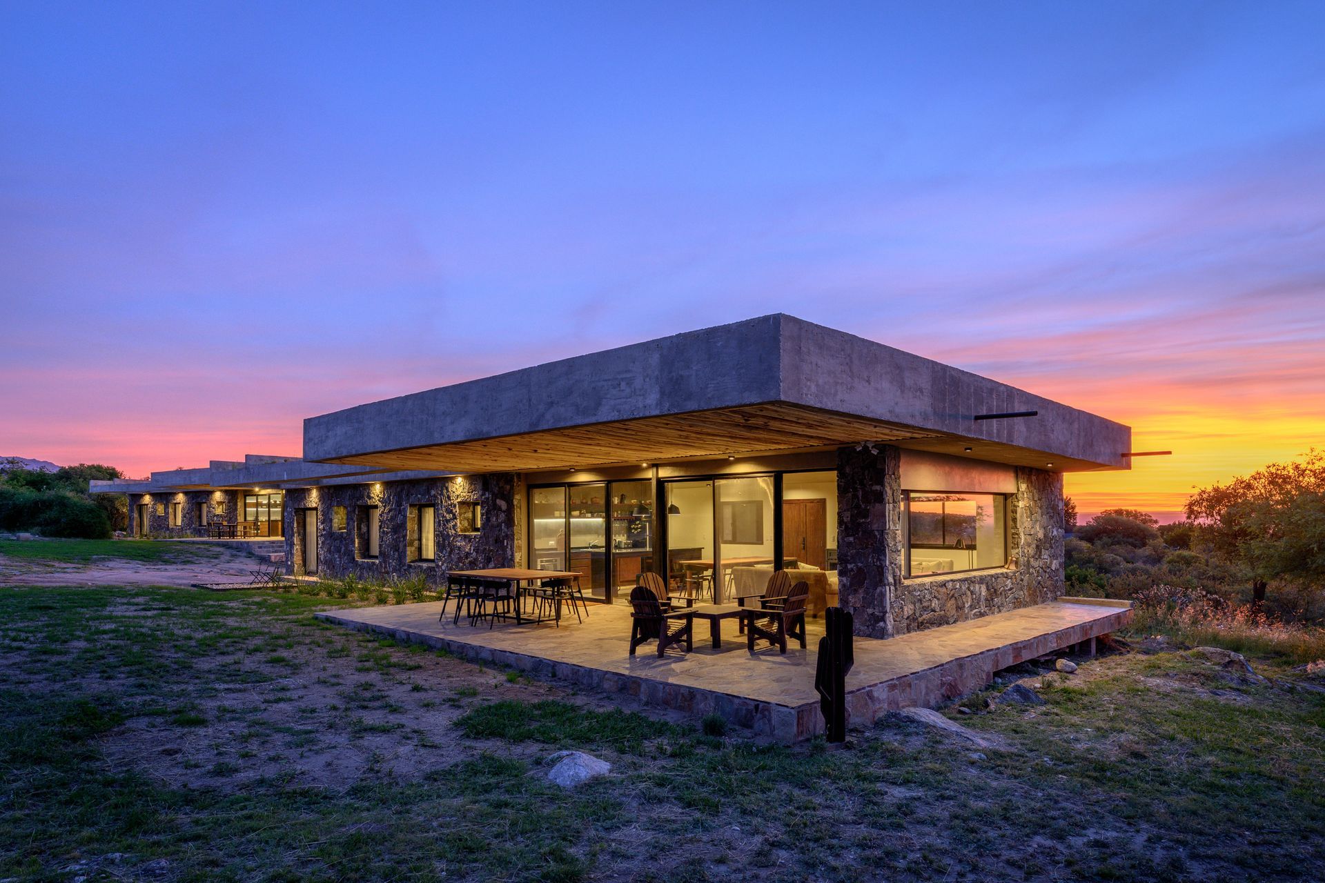 Cabaña de piedra moderna con vista al atardecer, zona de estar al aire libre.