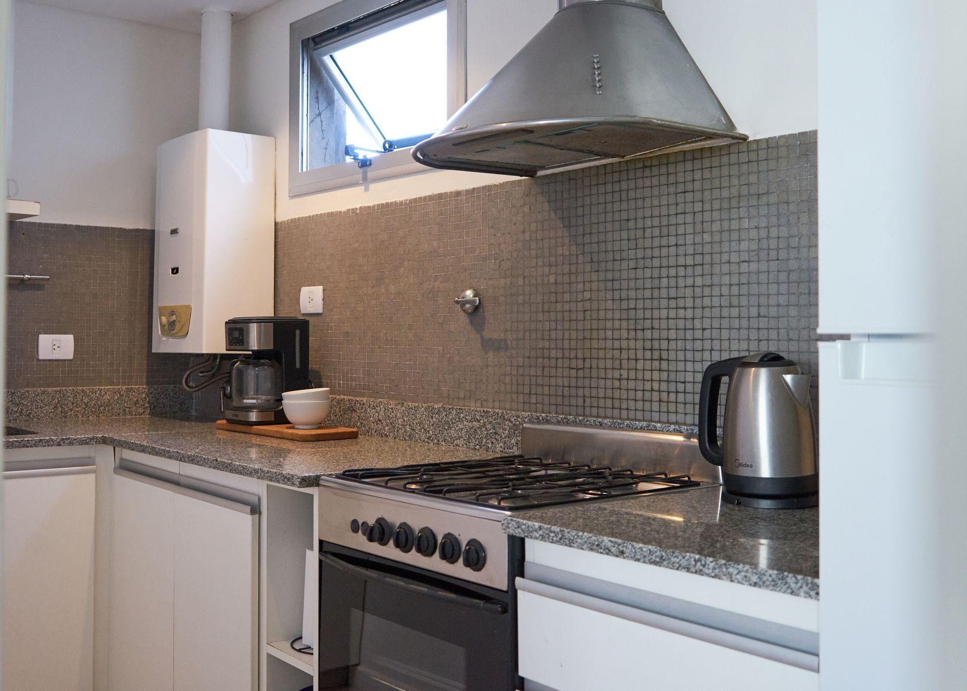 Cocina con estufa, encimera, gabinetes, campana extractora y calentador de agua.