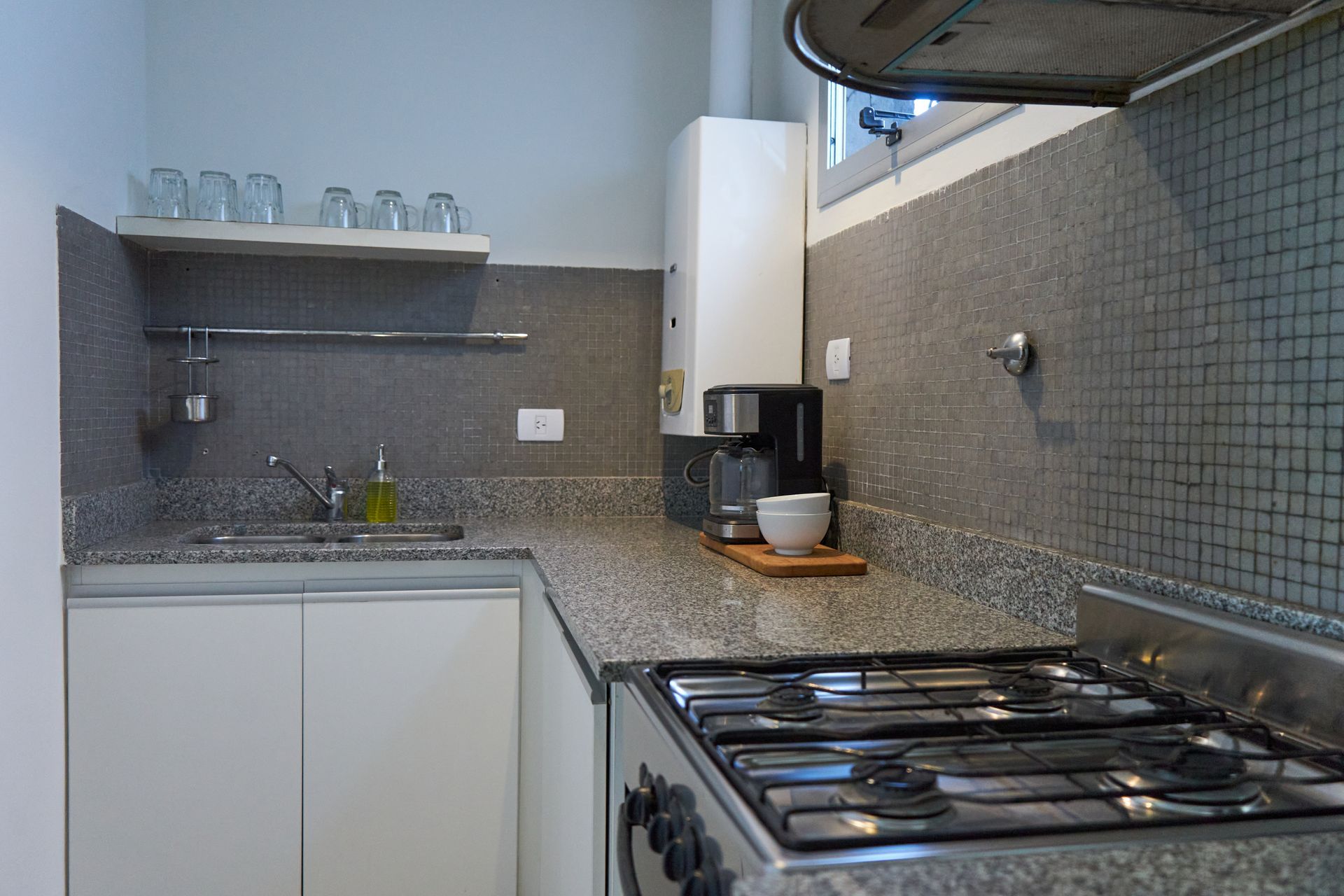 Cocina pequeña con estufa, encimera, gabinetes, fregadero y cafetera.