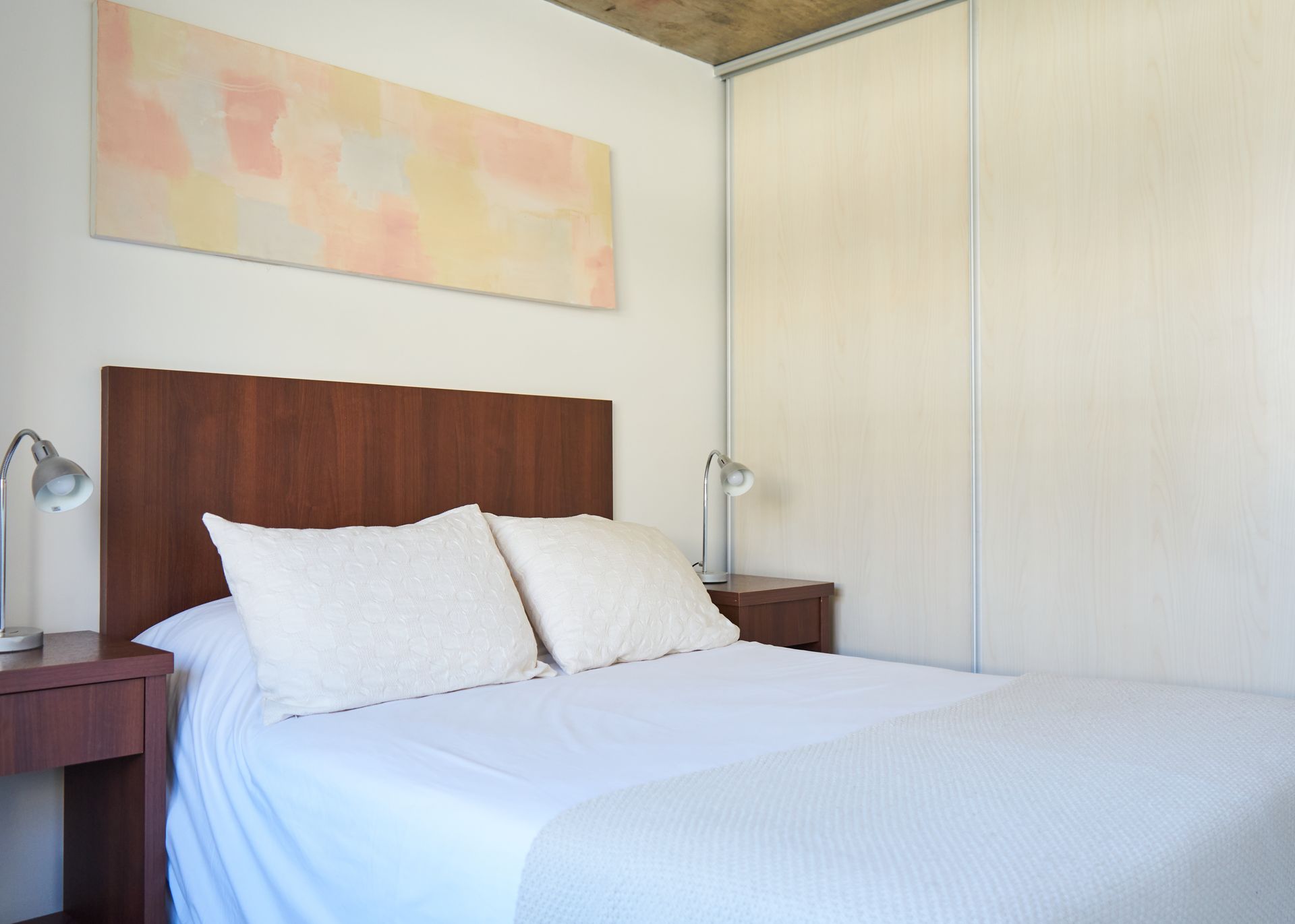 Dormitorio con cama, mesitas de noche, lámparas, cabecero, armario y un cuadro.