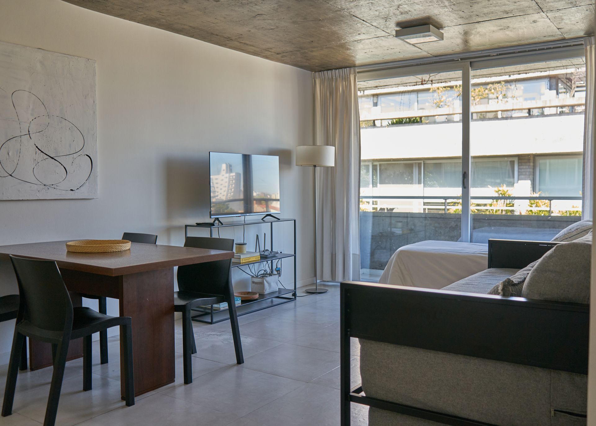 Interior de apartamento moderno con mesa de comedor, TV, sofá y vista al balcón.
