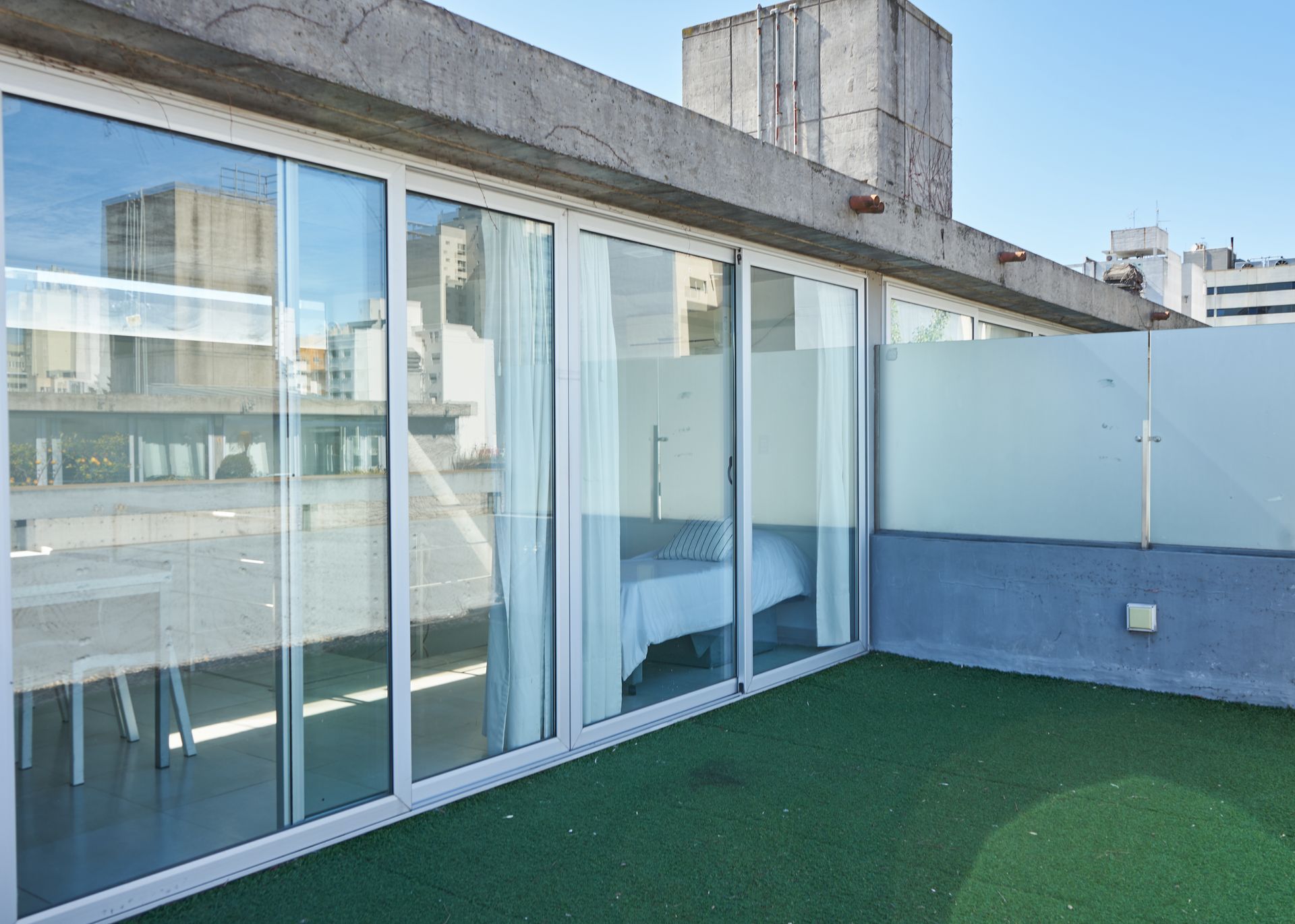 Habitación con paredes de cristal y una cama que da a un patio en la azotea y barrera de vidrio esmerilado.