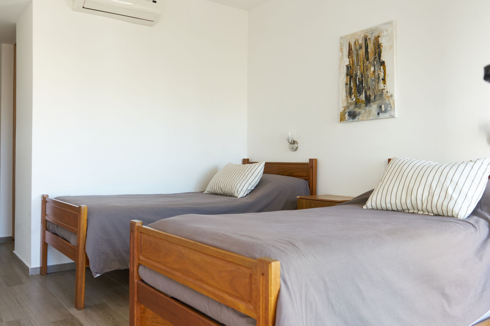 Dos camas individuales con ropa de cama gris en una habitación de paredes blancas.