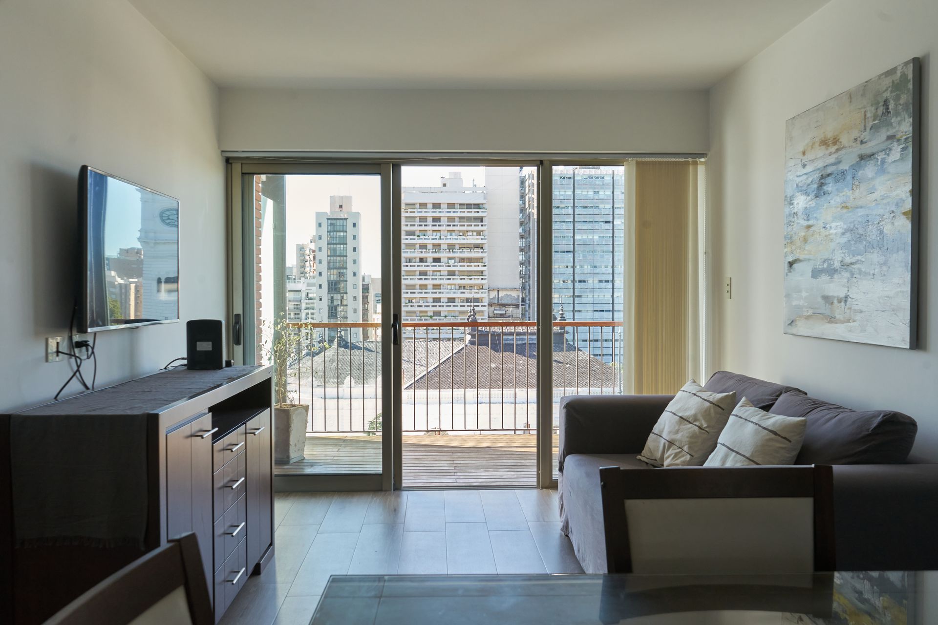 Sala de estar con sofá oscuro, TV y vista a la ciudad a través de puertas corredizas de vidrio.