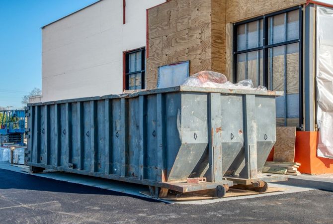 Large metal dumpster bins beside a warehouse wall on an industrial lot.