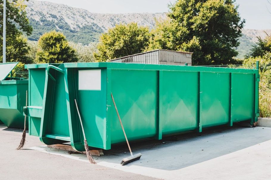 Large green dumpster on a paved area with mountains and trees in the background