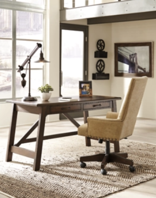 Modern home office with dark wood desk, beige chair, table lamp, and wall mirror on a light rug.