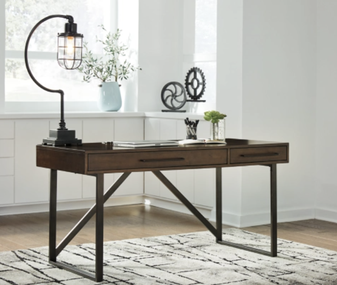 Modern dark wood desk with black lamp in a bright, minimalist room with plants and a patterned rug