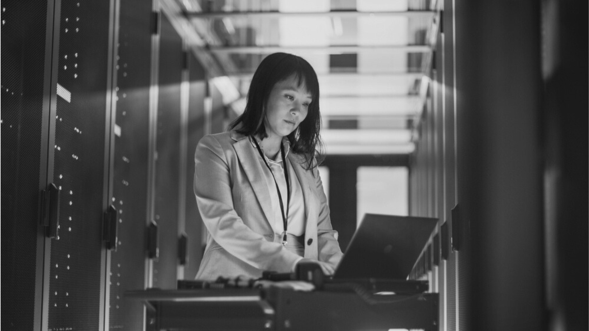 a woman is standing in a server room using a laptop computer .