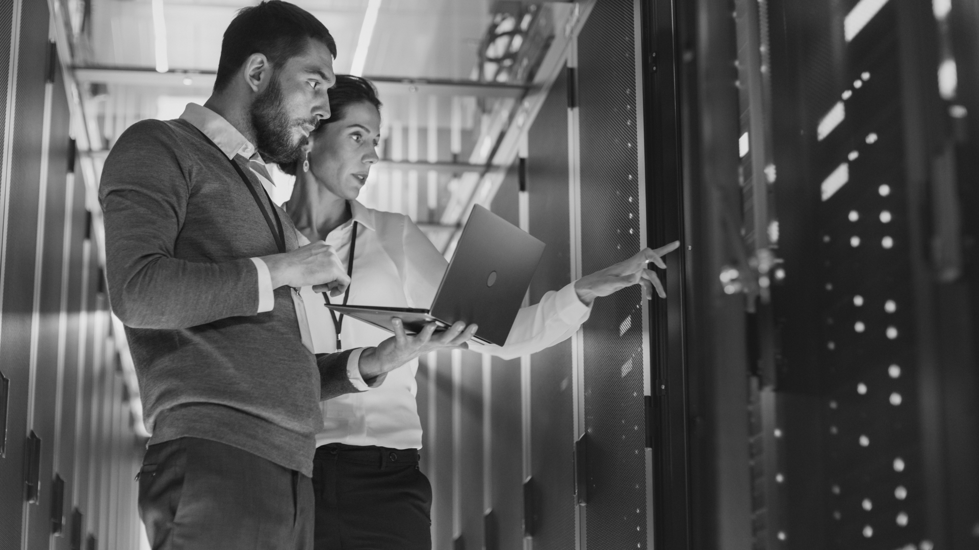 a man and a woman are looking at a laptop in a server room working on IT compliance.