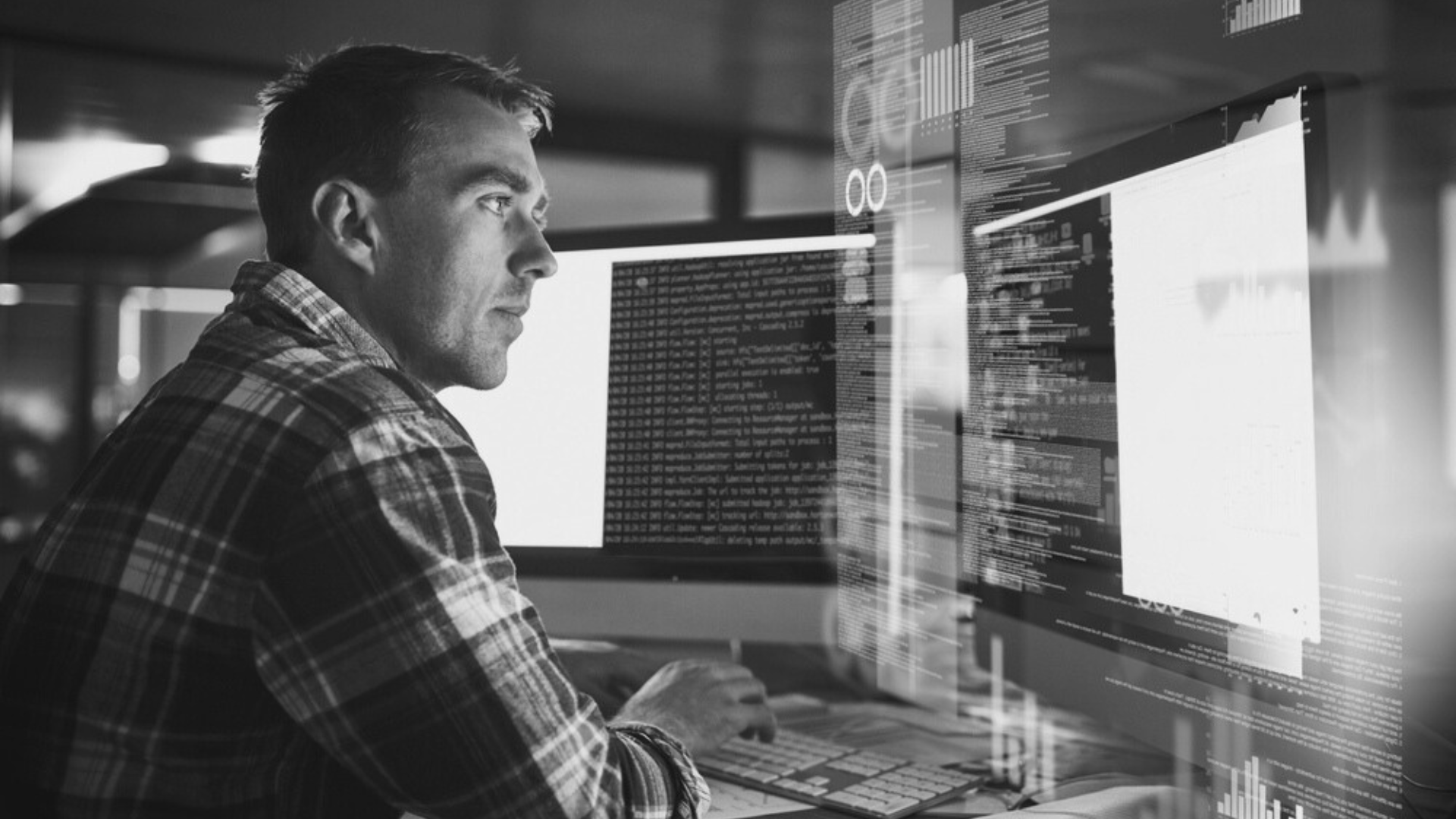A man is sitting in front of two computer monitors.