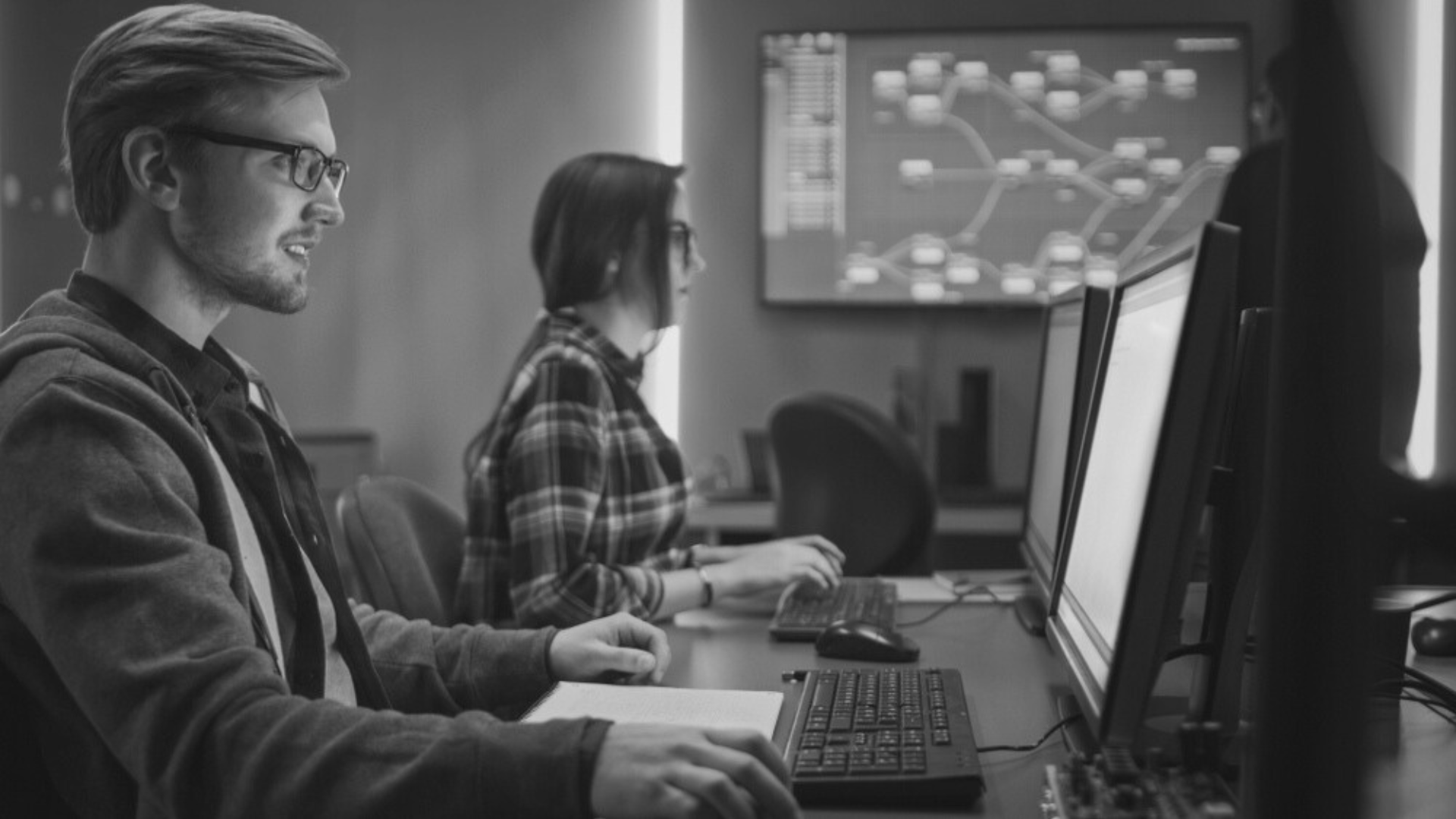 a man and a woman are sitting at a desk in front of computer monitors.