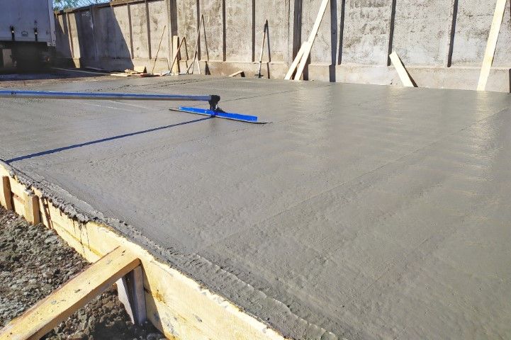Freshly poured gray concrete slab with blue leveling tool on top at a construction site