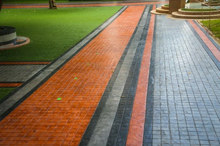 Rainy park walkway with orange and blue brick paths beside green grass