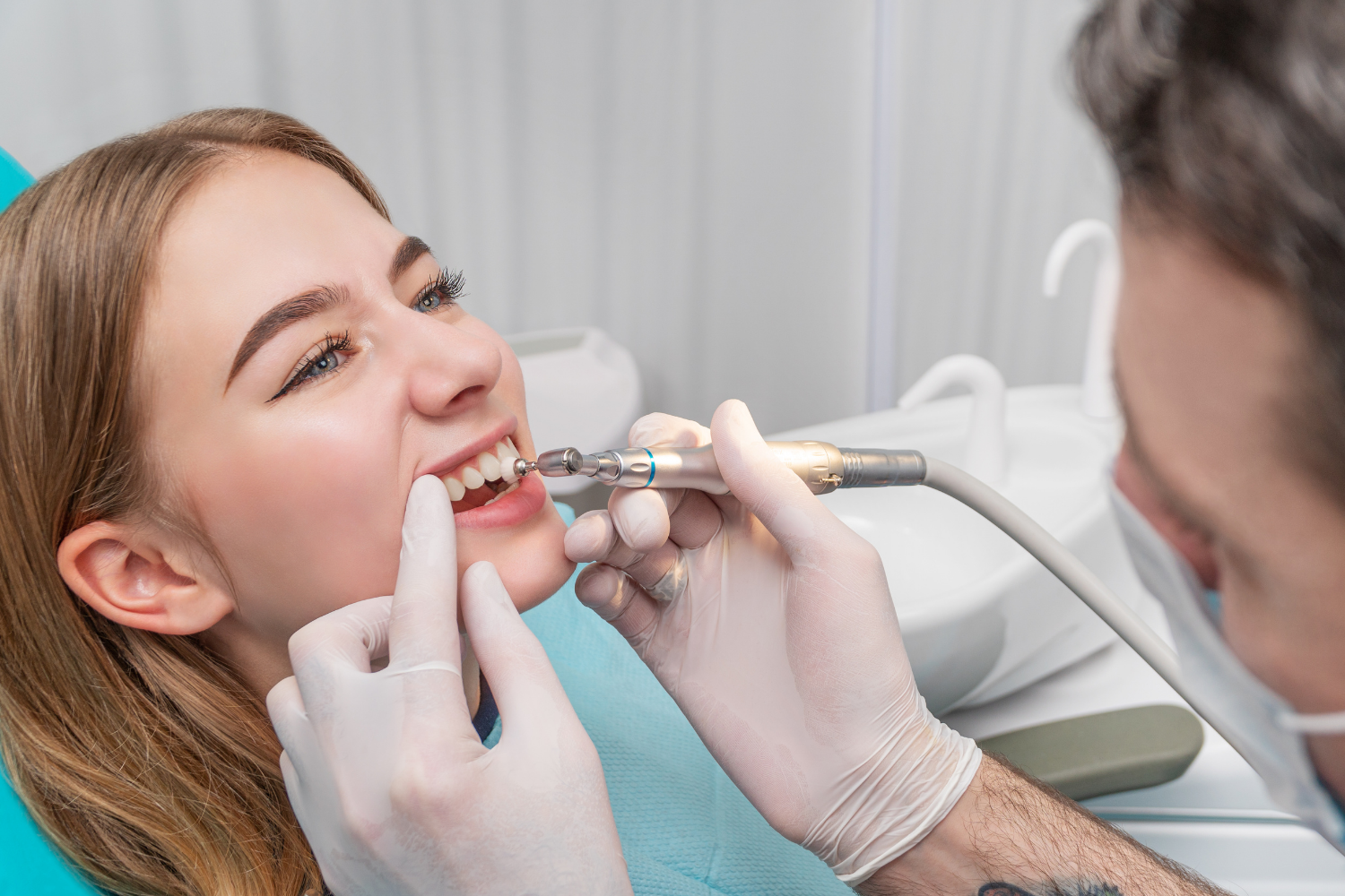 A gloved professional points to a specific area on a panoramic dental X-ray displayed on a screen.