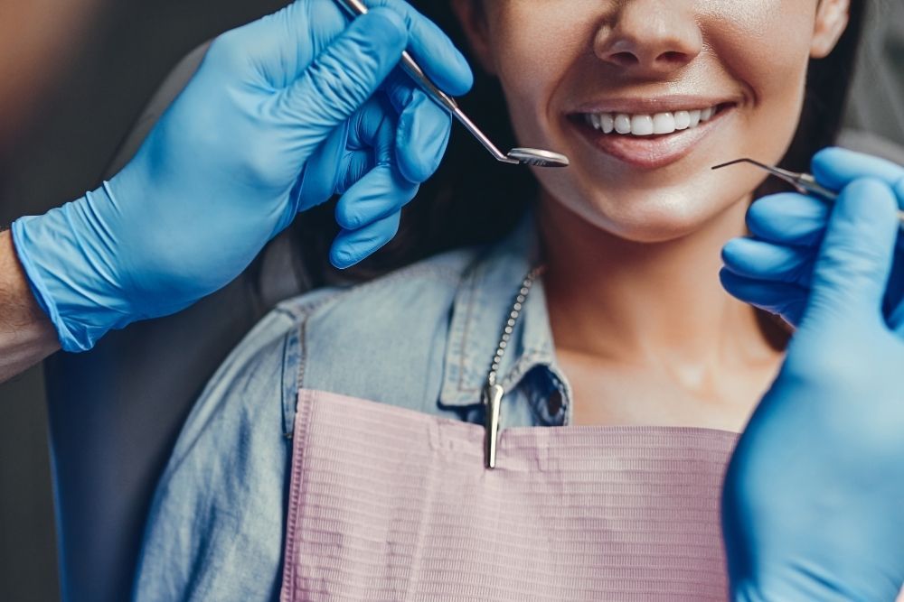 A gloved professional points to a specific area on a panoramic dental X-ray displayed on a screen.