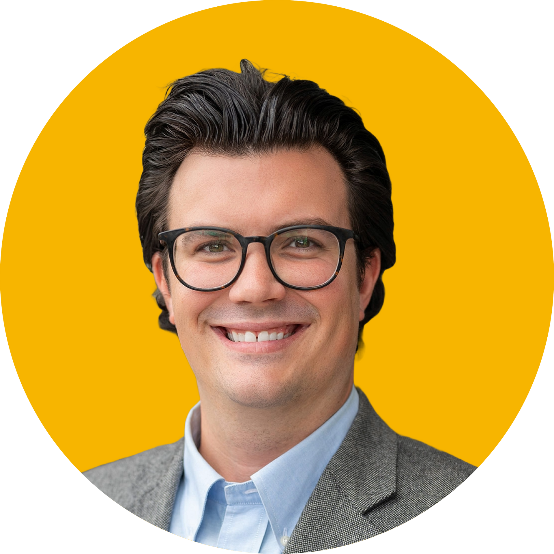 A person with dark hair and glasses smiles while wearing a light blue collared shirt and gray blazer against a yellow disc.
