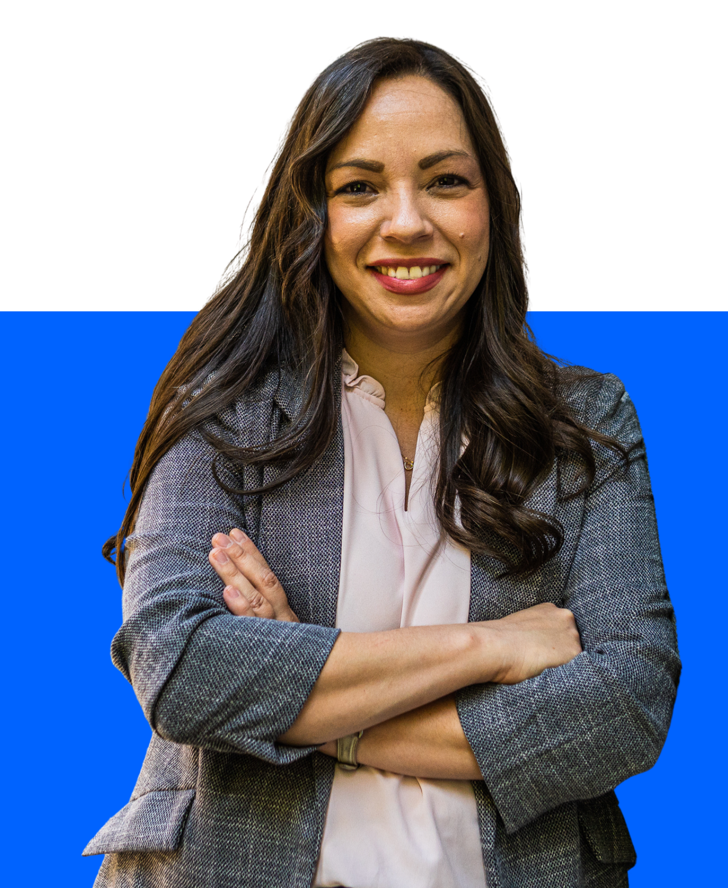 A person with long, wavy brown hair smiling, wearing a white shirt and a gray textured blazer against a blue background.
