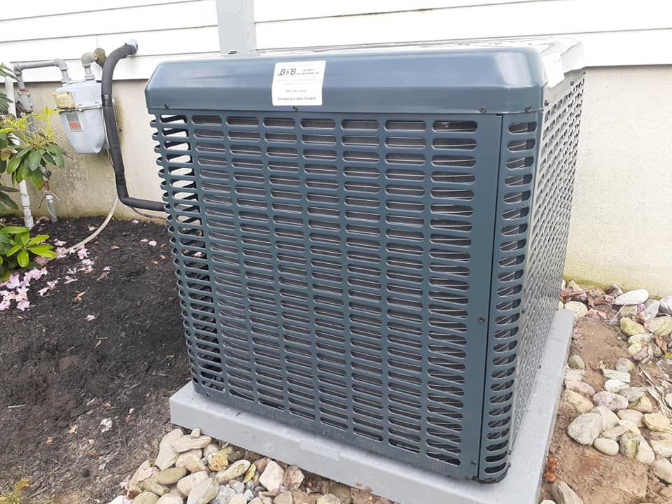 Gray HVAC unit outside a building, on a concrete base, near rocks and a gas meter.