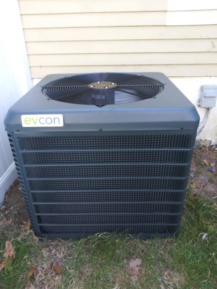 Evcon air conditioning unit outside, gray and black, next to a wall.