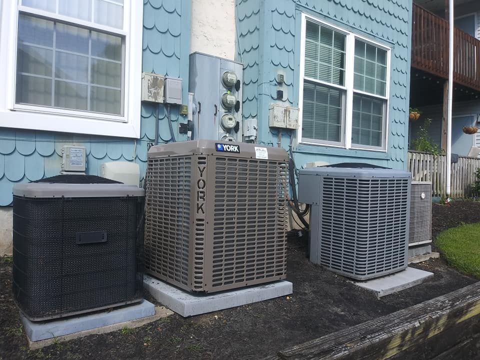 Air conditioning units lined up against a light blue building with white windows.