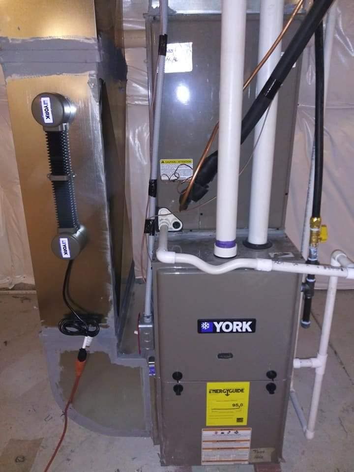 A York furnace in a basement setting with ductwork and piping. The unit is gray with a yellow energy label.