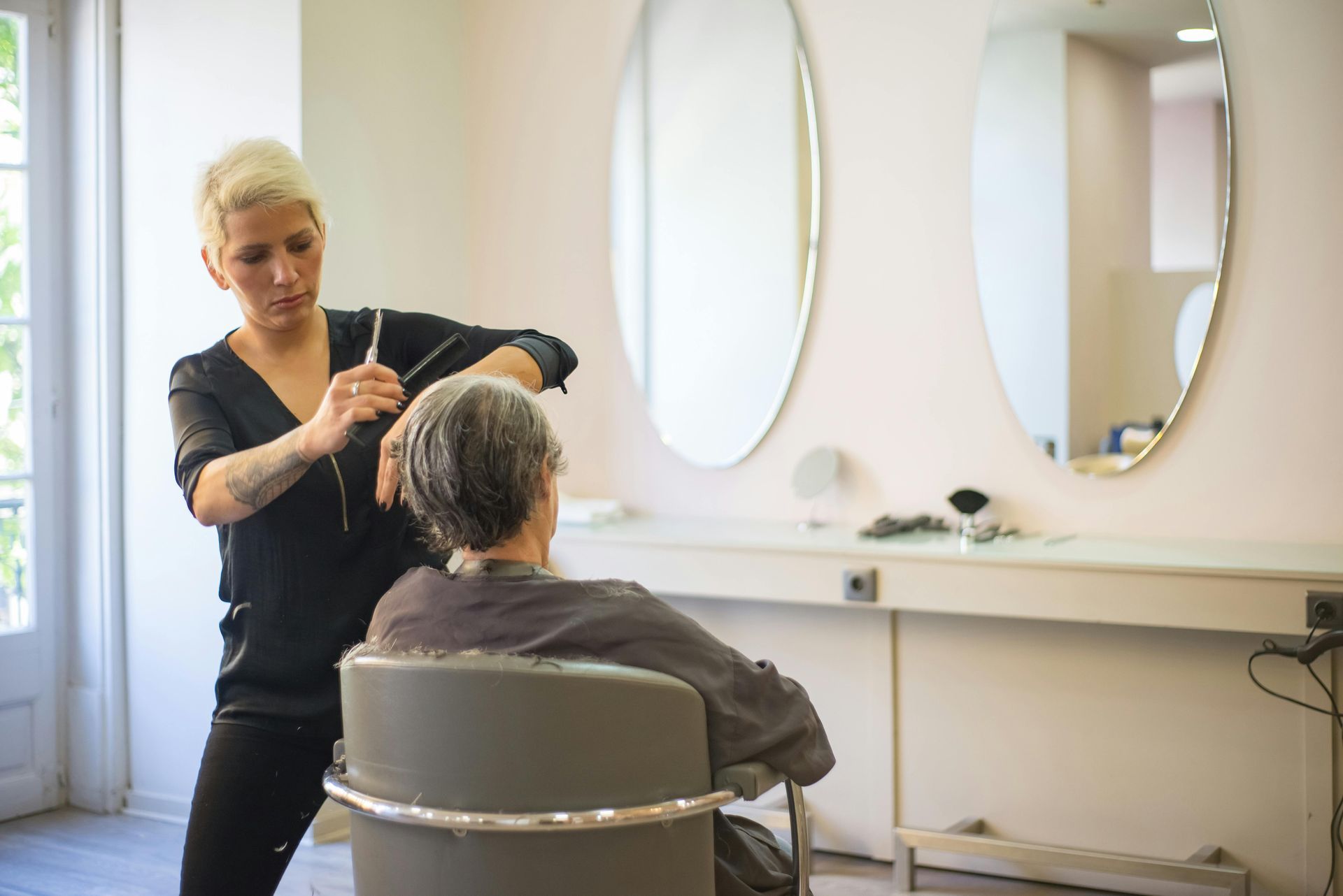 Stylist cutting a seated client’s hair in a bright salon with mirrors and a styling station
